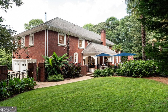 back of house with a lawn, roof with shingles, an attached garage, brick siding, and a chimney