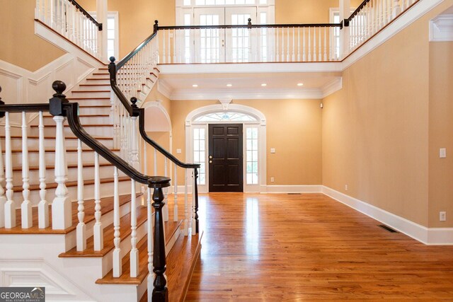 foyer with visible vents, baseboards, ornamental molding, a towering ceiling, and wood finished floors