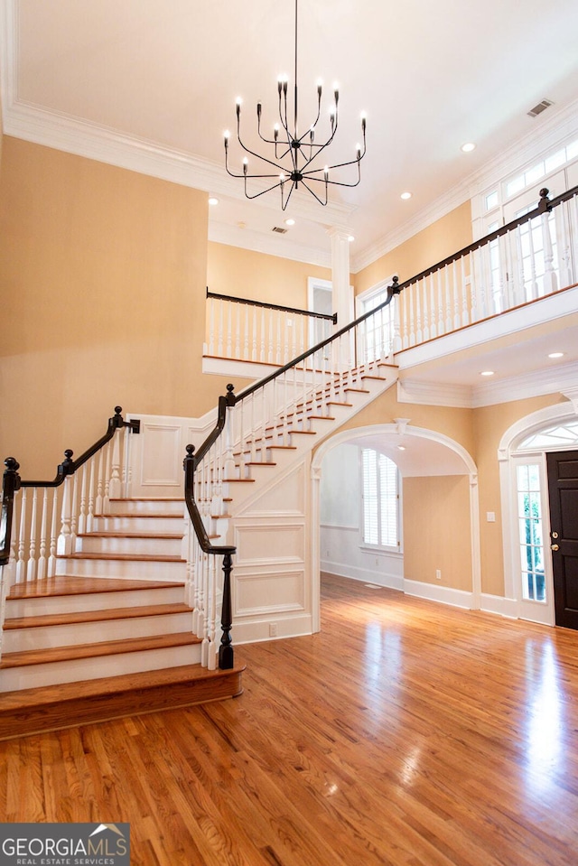 stairs featuring wood finished floors, arched walkways, a chandelier, and crown molding