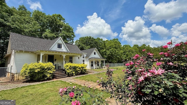 view of front of property with fence, roof with shingles, a porch, and a front lawn