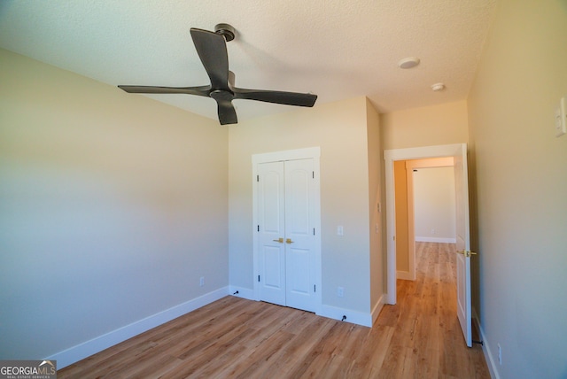 unfurnished bedroom with wood finished floors, a textured ceiling, a closet, ceiling fan, and baseboards