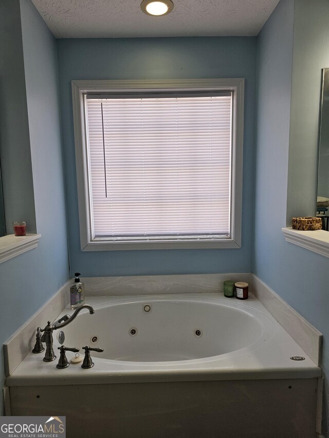 bathroom with a wealth of natural light, a textured ceiling, and a whirlpool tub