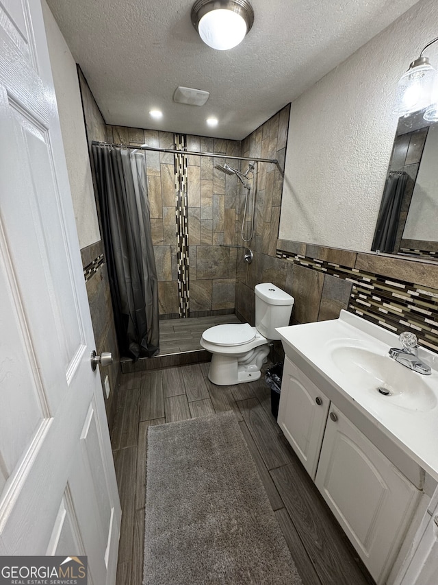 full bathroom featuring wood finish floors, a textured ceiling, toilet, tile walls, and a tile shower