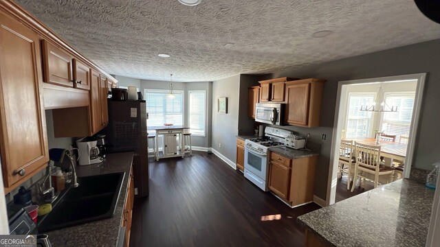 kitchen featuring stainless steel microwave, white gas range oven, dark countertops, brown cabinets, and a sink