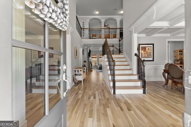 foyer entrance featuring crown molding, light wood finished floors, stairway, and a towering ceiling