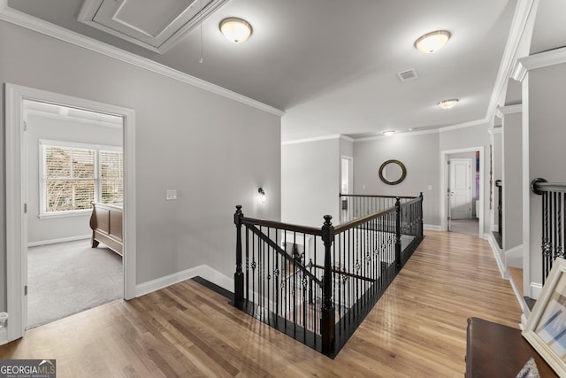 hallway with visible vents, ornamental molding, baseboards, and an upstairs landing