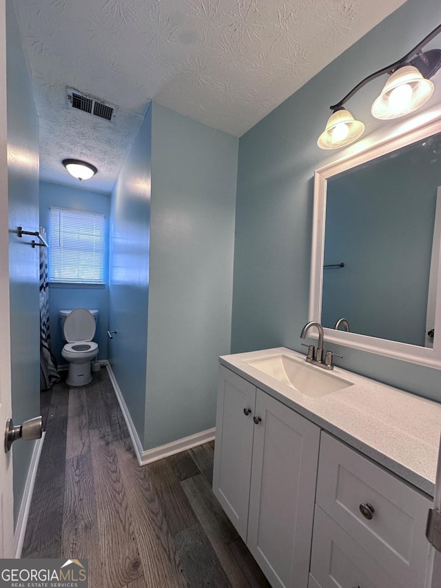 bathroom featuring visible vents, toilet, a textured ceiling, wood finished floors, and vanity