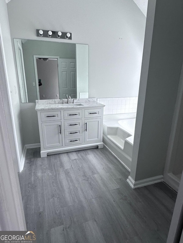 full bathroom with vanity, a bath, wood finished floors, and baseboards