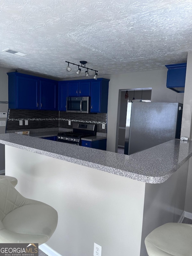 kitchen with blue cabinetry, stainless steel appliances, a kitchen bar, and a textured ceiling