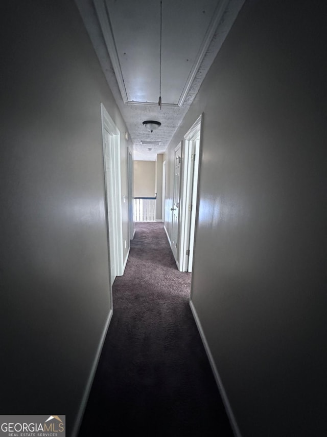 corridor with attic access, baseboards, and dark carpet