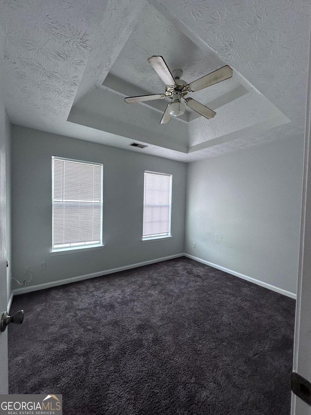 empty room featuring baseboards, visible vents, a textured ceiling, a raised ceiling, and dark carpet