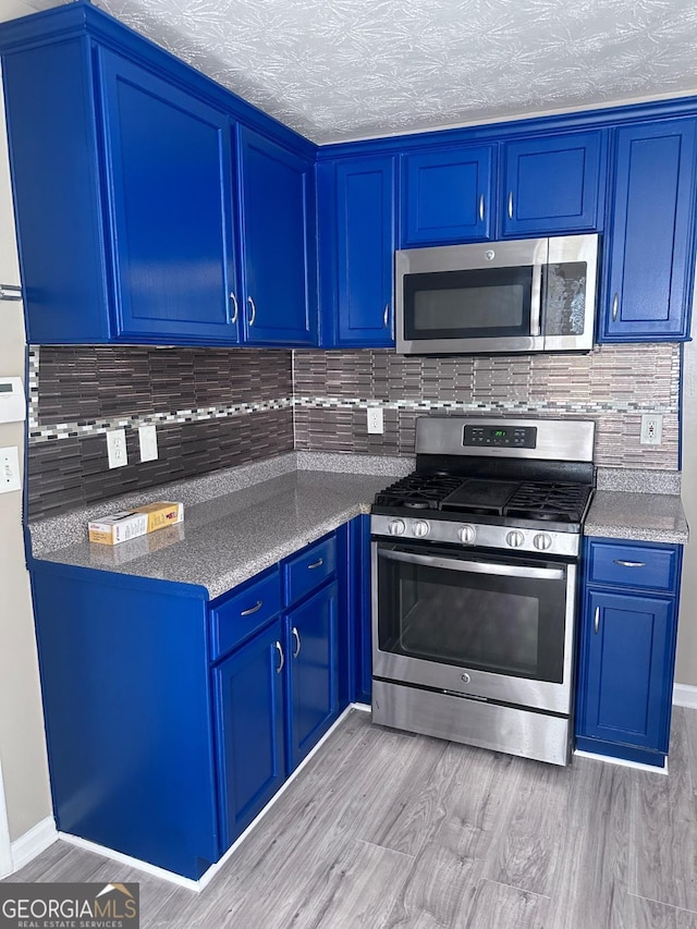 kitchen with tasteful backsplash, blue cabinetry, appliances with stainless steel finishes, and light wood-style flooring