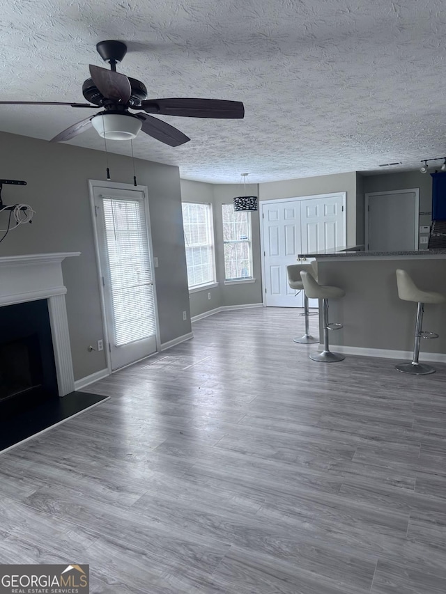 unfurnished living room featuring wood finished floors, baseboards, a fireplace with raised hearth, ceiling fan, and a textured ceiling