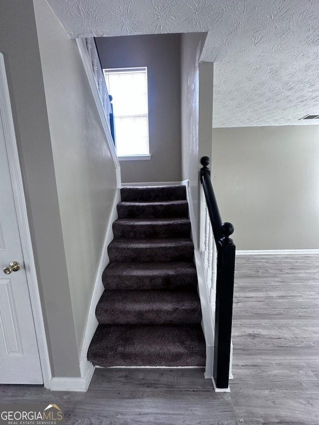 stairway with baseboards, wood finished floors, visible vents, and a textured ceiling