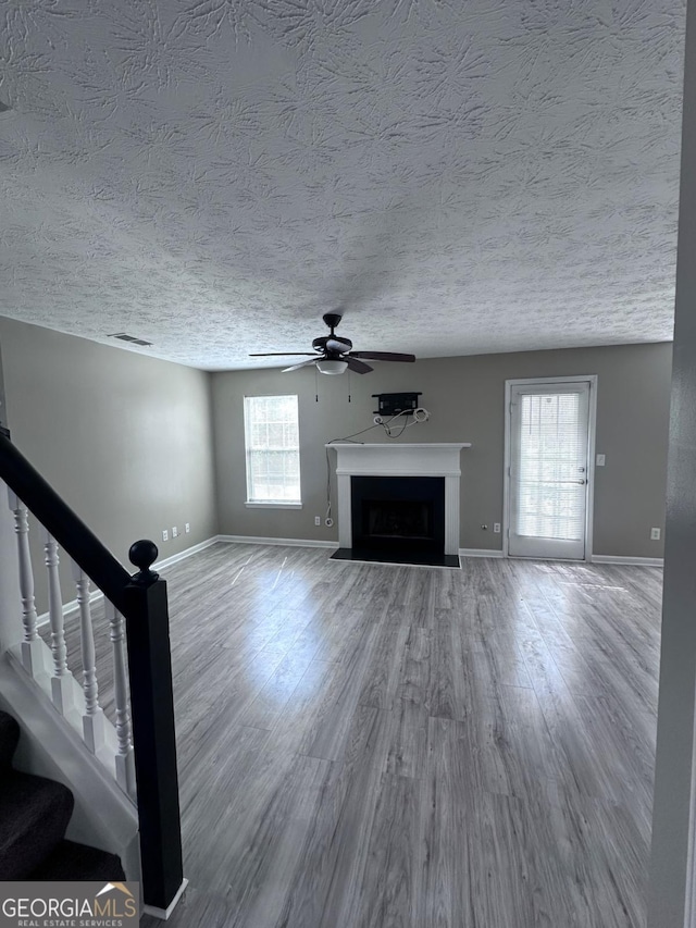 unfurnished living room with baseboards, ceiling fan, a fireplace with flush hearth, stairs, and wood finished floors