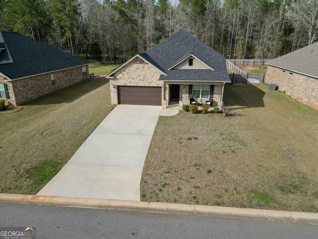 view of front of home with driveway, fence, roof with shingles, a front yard, and a garage