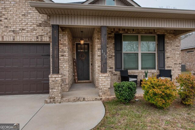 doorway to property featuring brick siding, a porch, concrete driveway, and an attached garage