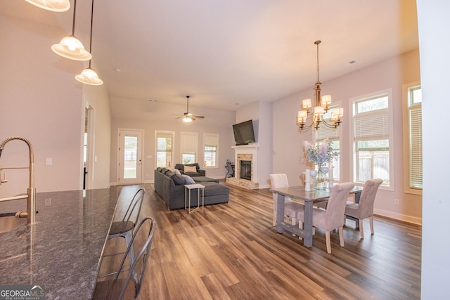 dining space featuring plenty of natural light, a fireplace with raised hearth, ceiling fan with notable chandelier, and wood finished floors