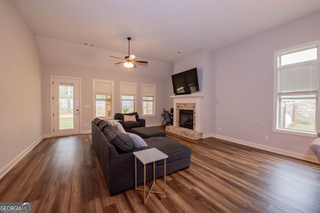 living area with a fireplace with raised hearth, ceiling fan, baseboards, and dark wood-style flooring
