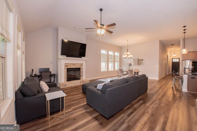 living area featuring dark wood-style floors, ceiling fan with notable chandelier, a brick fireplace, and baseboards