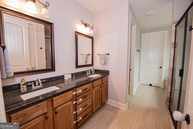 full bathroom featuring double vanity, a shower stall, baseboards, and a sink