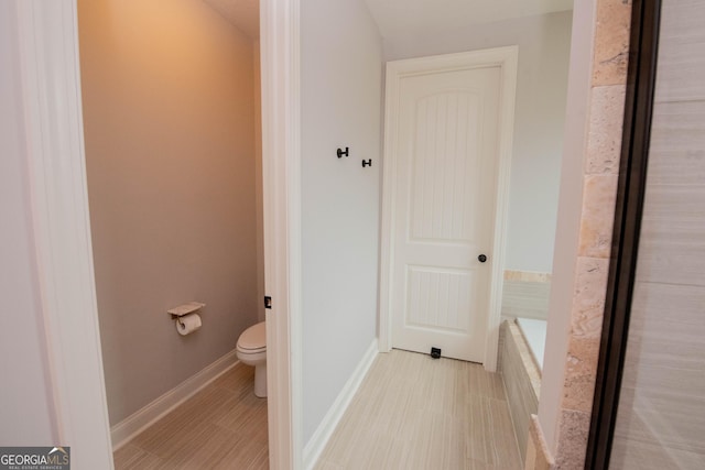 bathroom with baseboards, toilet, and tiled tub