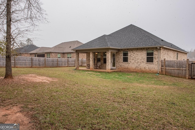 rear view of property with roof with shingles, a fenced backyard, a lawn, a patio area, and brick siding