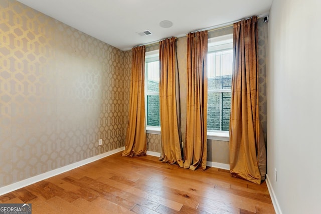 spare room with light wood-style flooring, wallpapered walls, and a healthy amount of sunlight