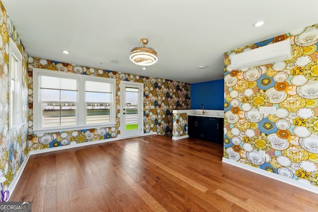 unfurnished living room featuring wallpapered walls, baseboards, a sink, and wood finished floors