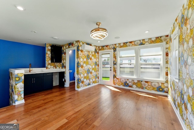 interior space with baseboards, wallpapered walls, a wall mounted air conditioner, light wood-style flooring, and light countertops