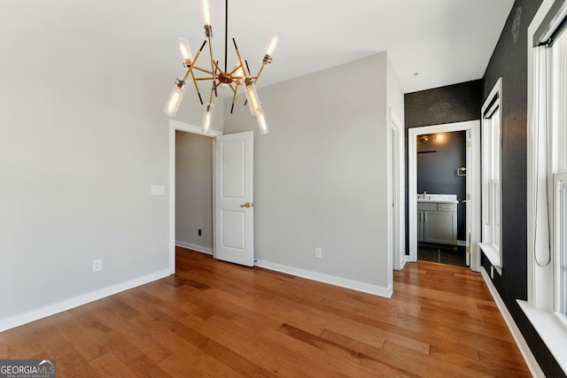 unfurnished dining area with light wood-style flooring, an inviting chandelier, and baseboards