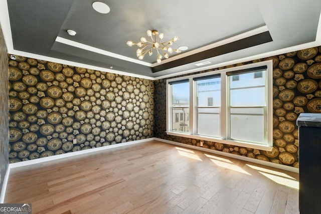 spare room with baseboards, a raised ceiling, an inviting chandelier, wallpapered walls, and wood-type flooring