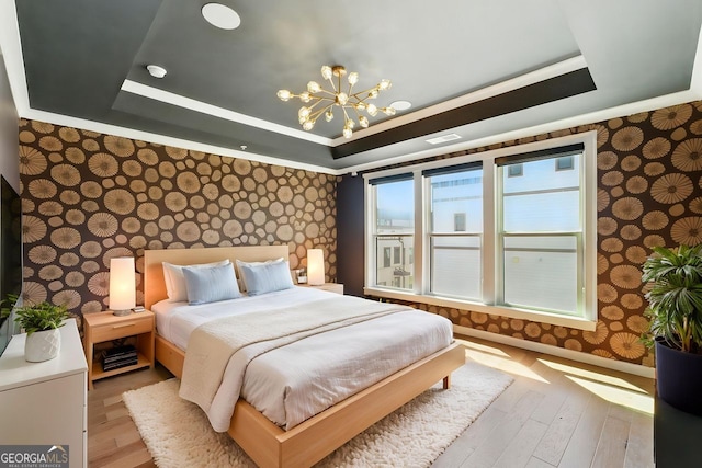 bedroom with hardwood / wood-style flooring, an inviting chandelier, wallpapered walls, and a raised ceiling