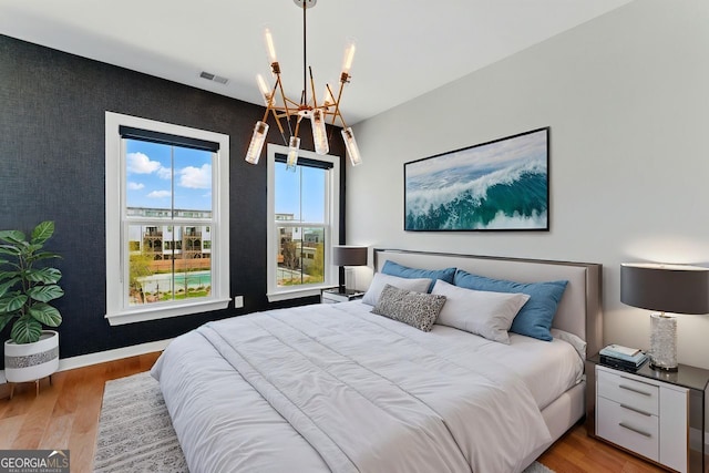 bedroom with a chandelier, wood finished floors, visible vents, and baseboards