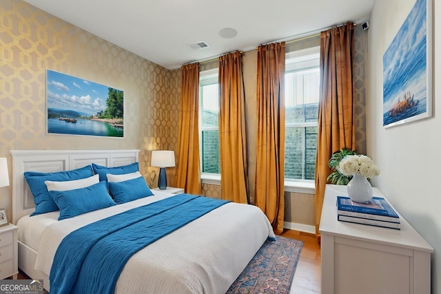 bedroom featuring light wood-type flooring, wallpapered walls, baseboards, and visible vents