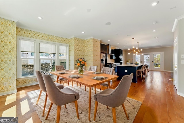 dining room with light wood-style flooring, baseboards, a chandelier, wallpapered walls, and crown molding