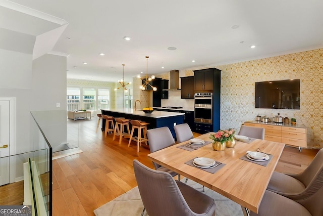 dining space with an inviting chandelier, crown molding, light wood finished floors, and wallpapered walls