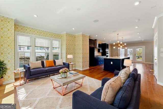 living area featuring a chandelier, wallpapered walls, light wood-style floors, and ornamental molding