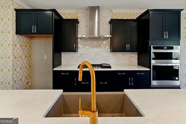 kitchen with stainless steel appliances, dark cabinets, wall chimney exhaust hood, and a sink