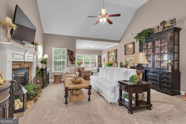 living area with high vaulted ceiling, carpet floors, ceiling fan, baseboards, and a stone fireplace