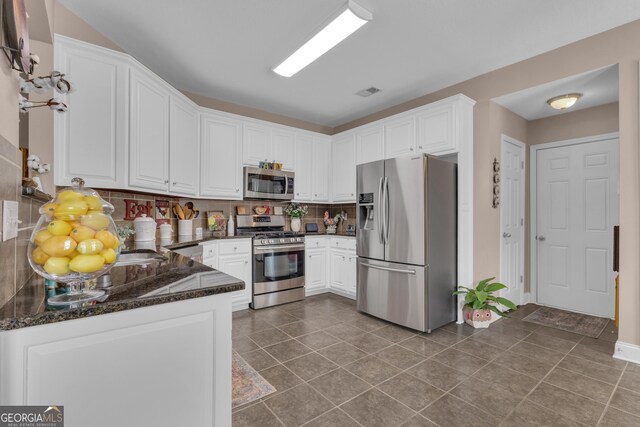 kitchen featuring stainless steel appliances, tasteful backsplash, white cabinetry, dark stone counters, and dark tile patterned floors