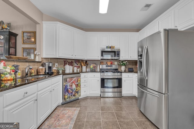 kitchen featuring appliances with stainless steel finishes, a sink, white cabinets, and tasteful backsplash