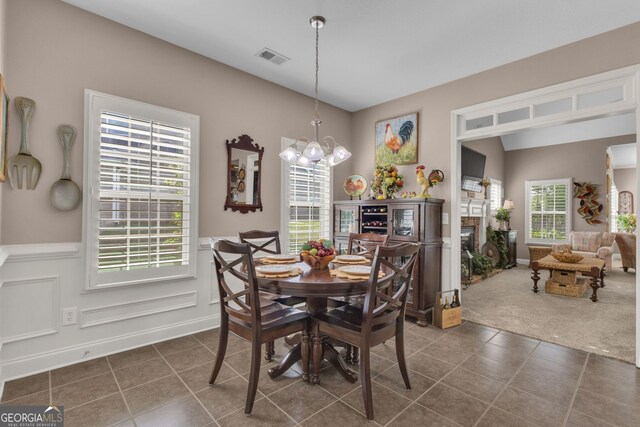 dining area featuring dark tile patterned flooring, plenty of natural light, a glass covered fireplace, and a wainscoted wall