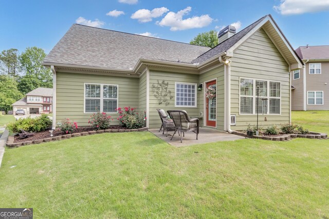 back of house with a patio, a chimney, a lawn, and a shingled roof