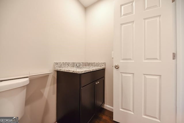 half bath with baseboards, toilet, and vanity