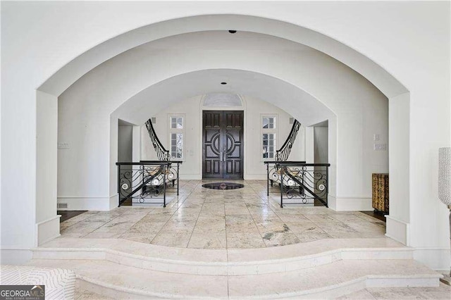 entrance foyer with baseboards, marble finish floor, stairs, and arched walkways