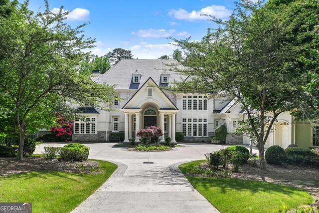 view of front of home with curved driveway, stucco siding, stone siding, and a chimney