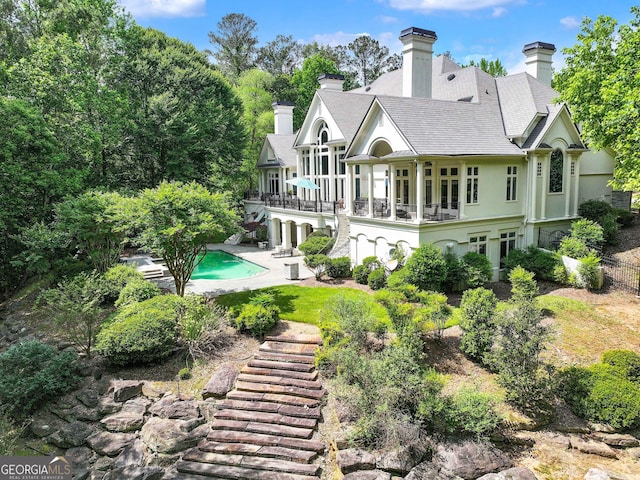 back of property with a patio, an outdoor pool, stucco siding, a chimney, and stairs