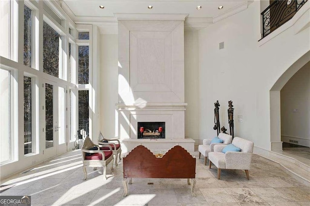 sitting room featuring crown molding, a high ceiling, recessed lighting, arched walkways, and a premium fireplace