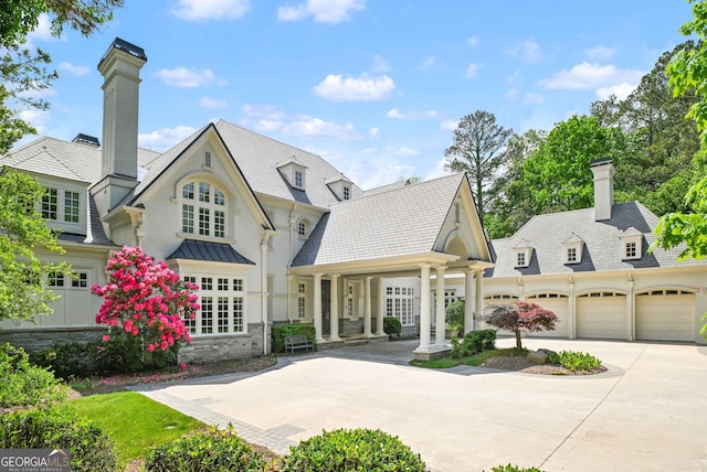 view of front of house with an attached garage, stone siding, a chimney, covered porch, and driveway